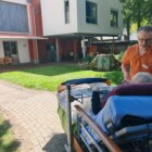 ein Hospizgast im Krankenbett im Garten betreut von einer Pflegekraft